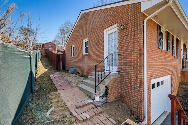 view of side of home with brick siding, entry steps, a garage, and fence