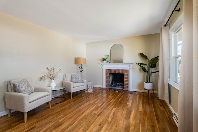 living area with a brick fireplace, a baseboard heating unit, baseboards, and wood finished floors