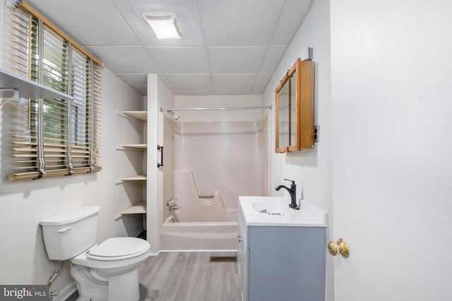 full bathroom with hardwood / wood-style floors, a paneled ceiling, vanity, toilet, and washtub / shower combination