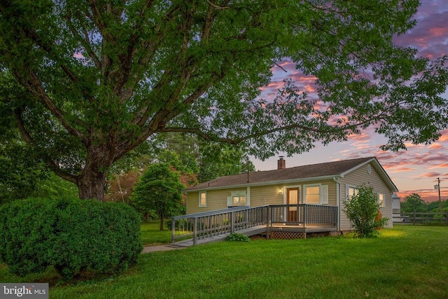 back house at dusk with a lawn and a deck