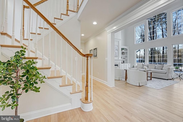 foyer featuring crown molding, a fireplace, a high ceiling, light wood-type flooring, and baseboards