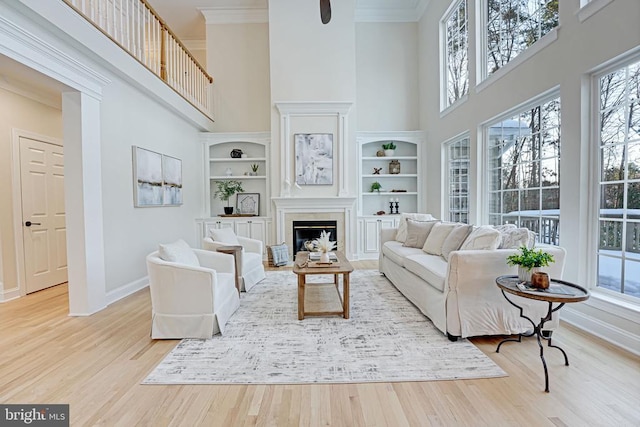 living area featuring a high ceiling, baseboards, light wood finished floors, a glass covered fireplace, and crown molding