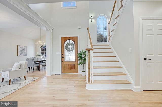 foyer entrance featuring stairs, light wood finished floors, baseboards, and an inviting chandelier