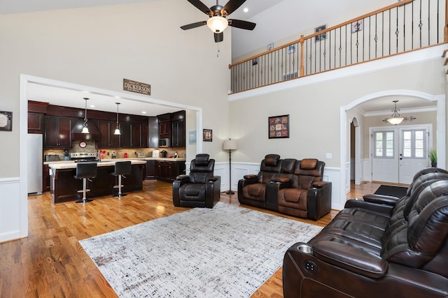 living area with ornamental molding, wainscoting, ceiling fan, light wood-type flooring, and arched walkways