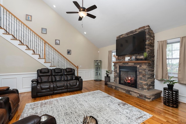 living room featuring a ceiling fan, a stone fireplace, wood finished floors, high vaulted ceiling, and stairs