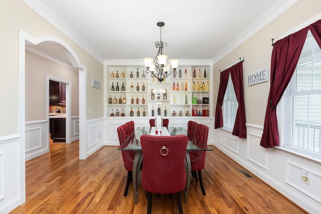 dining area with an inviting chandelier, light wood finished floors, arched walkways, visible vents, and ornamental molding