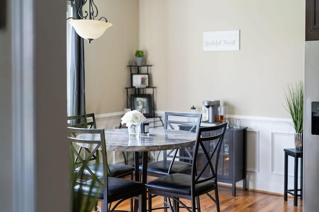 dining space with wood finished floors, a decorative wall, and a wainscoted wall