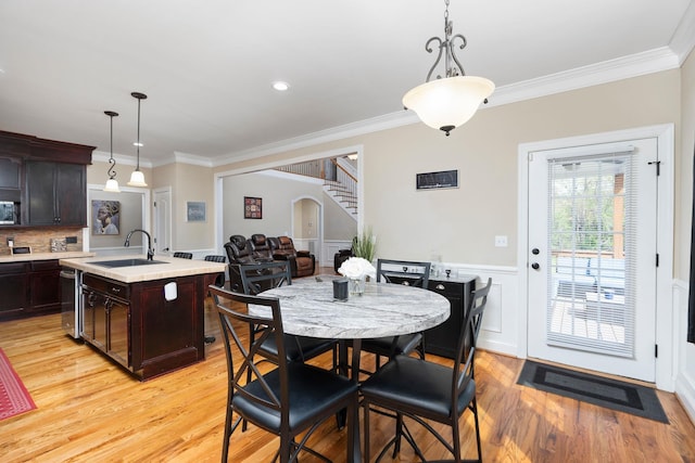 dining space featuring arched walkways, light wood-type flooring, a wainscoted wall, ornamental molding, and a decorative wall