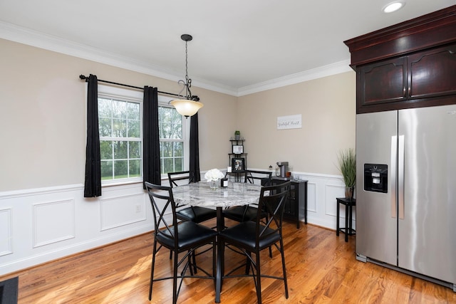 dining space with a wainscoted wall, ornamental molding, a decorative wall, and light wood-type flooring