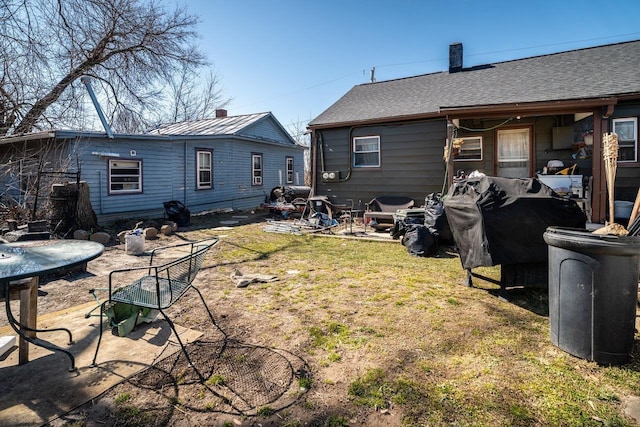 back of house featuring a patio area, a lawn, a chimney, and a shingled roof