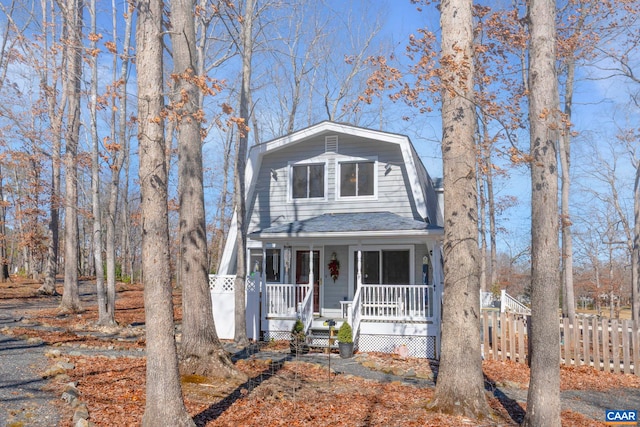 colonial inspired home with covered porch, a shingled roof, fence, and a gambrel roof