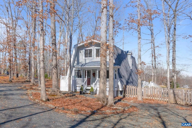 view of front of house with a porch, roof with shingles, fence, and a chimney