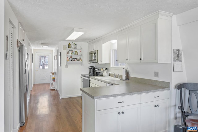 kitchen with appliances with stainless steel finishes, white cabinetry, a textured ceiling, and wood finished floors