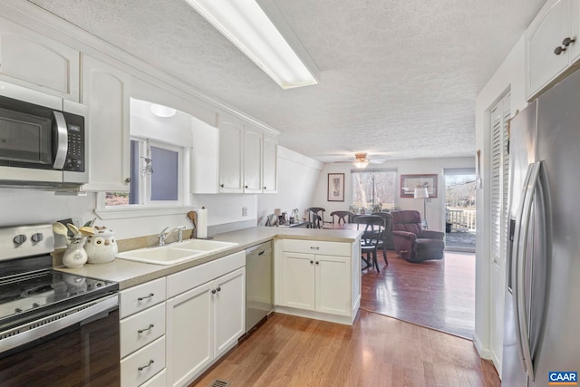 kitchen featuring stainless steel appliances, a peninsula, a sink, white cabinets, and light countertops