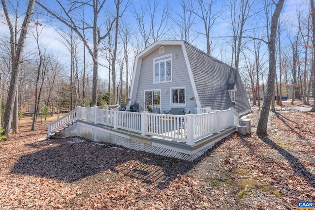 exterior space with a shingled roof, stairway, a deck, and a gambrel roof