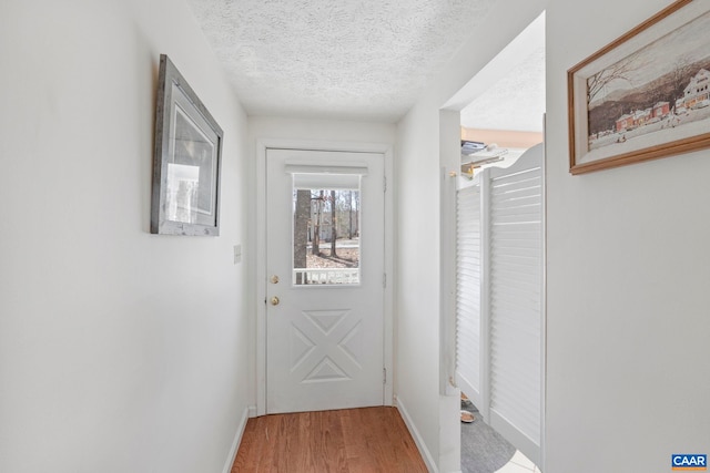 doorway with a textured ceiling, baseboards, and wood finished floors