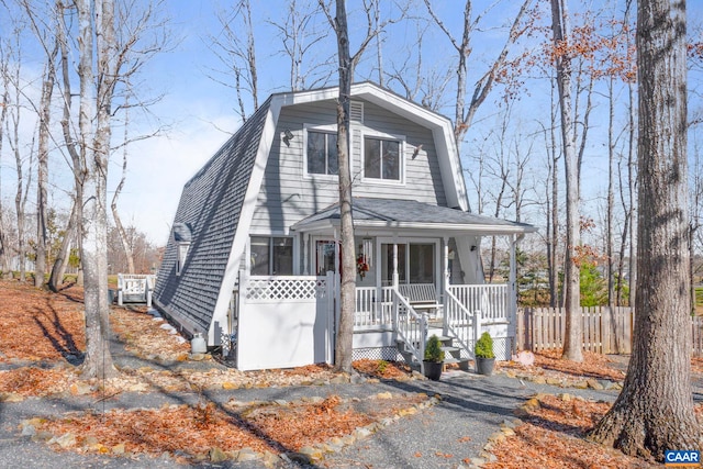 dutch colonial featuring a porch, roof with shingles, fence, and a gambrel roof