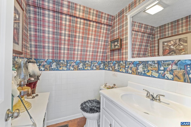 bathroom featuring a textured ceiling, wainscoting, vanity, and wallpapered walls