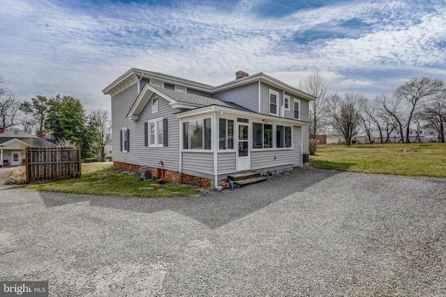 view of front of property with a front yard, a chimney, driveway, and a sunroom