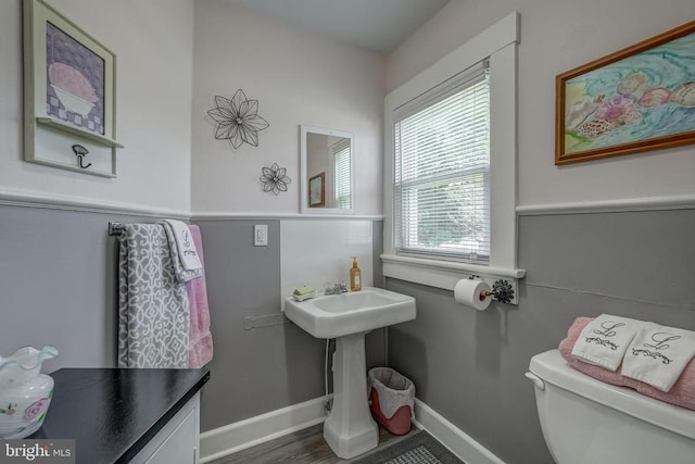 half bath with baseboards, toilet, and wood finished floors