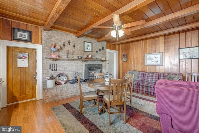 dining room featuring beamed ceiling, wood finished floors, wood walls, wood ceiling, and ceiling fan