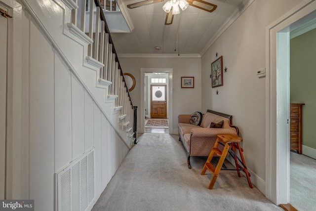 carpeted living room with visible vents, stairway, crown molding, baseboards, and ceiling fan