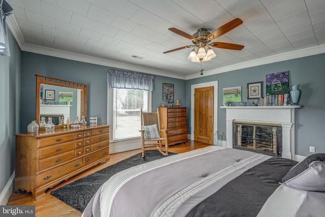 bedroom featuring crown molding, ceiling fan, baseboards, wood finished floors, and a glass covered fireplace