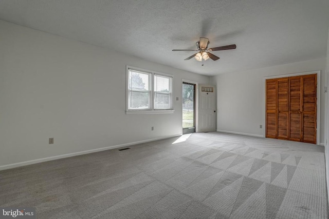 unfurnished room with baseboards, visible vents, ceiling fan, a textured ceiling, and light colored carpet