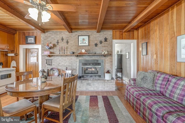 dining space with wooden walls, a brick fireplace, beam ceiling, wooden ceiling, and wood finished floors