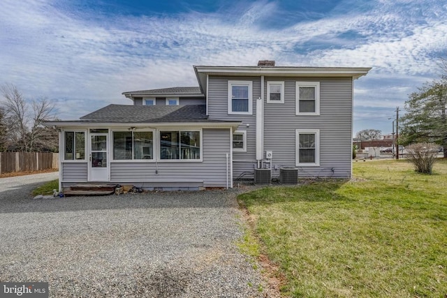 view of front of home with fence, a sunroom, a chimney, central air condition unit, and a lawn