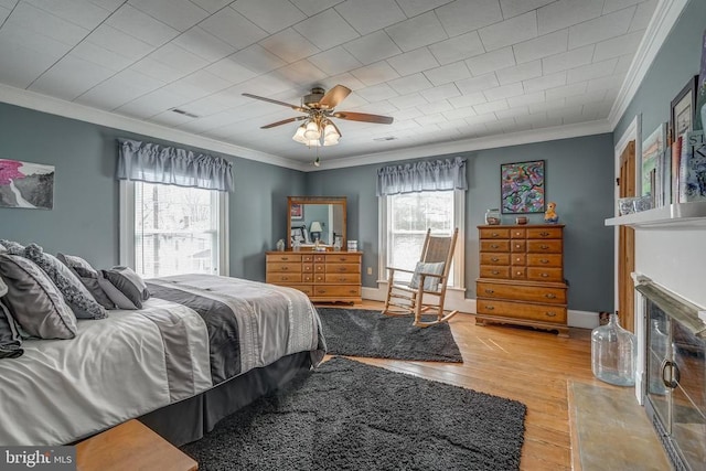 bedroom with a glass covered fireplace, light wood-style flooring, crown molding, and baseboards