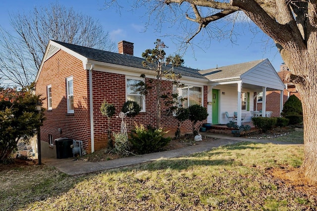 bungalow-style house with covered porch, brick siding, a chimney, and a front lawn