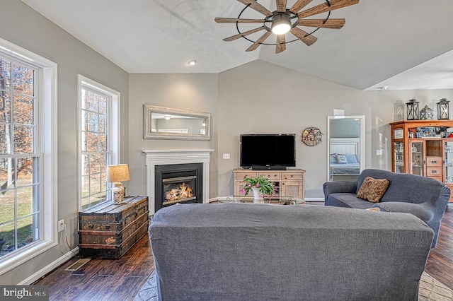 living room featuring vaulted ceiling, a lit fireplace, dark wood finished floors, and visible vents