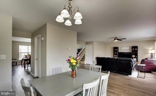 dining space with visible vents, ceiling fan with notable chandelier, wood finished floors, stairway, and baseboards