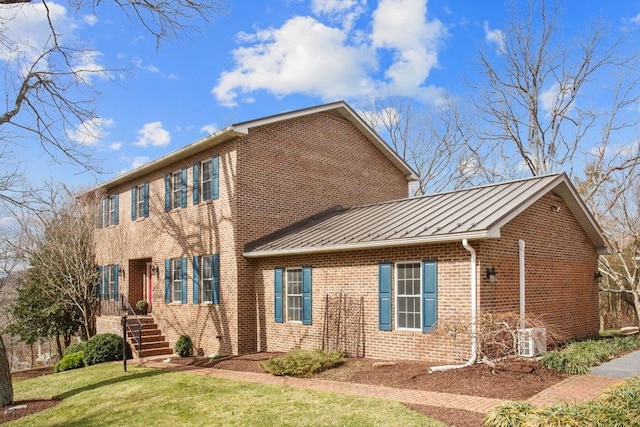 exterior space featuring brick siding, a front yard, a standing seam roof, metal roof, and stairs