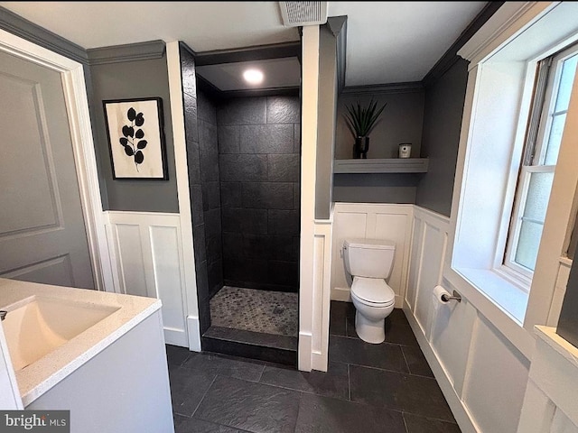 bathroom with toilet, a wainscoted wall, a tile shower, and a decorative wall