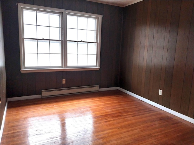 unfurnished room with light wood-style flooring, wooden walls, a baseboard heating unit, and baseboards