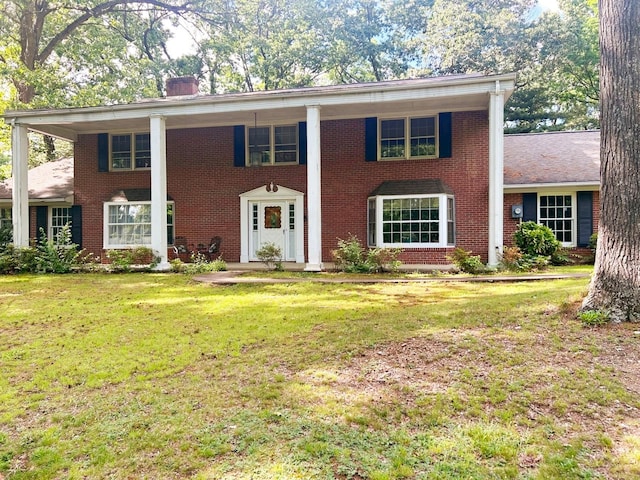 neoclassical / greek revival house featuring brick siding, a chimney, and a front yard