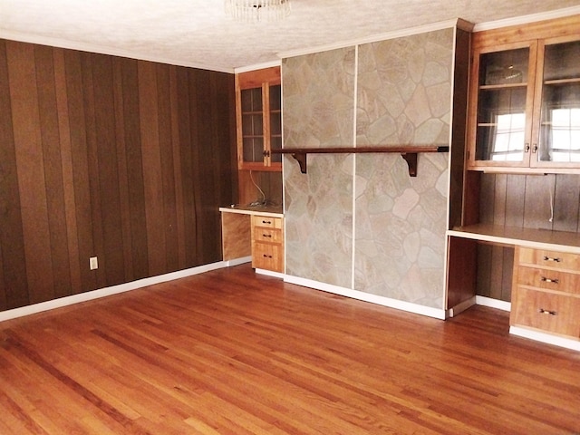 unfurnished room featuring wooden walls, baseboards, built in study area, dark wood-style floors, and ornamental molding