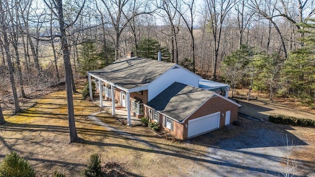 exterior space with gravel driveway, covered porch, a chimney, and a view of trees