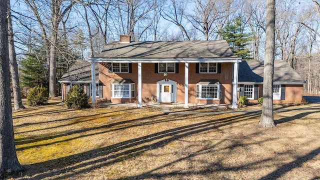 neoclassical / greek revival house with brick siding, a chimney, and a front lawn