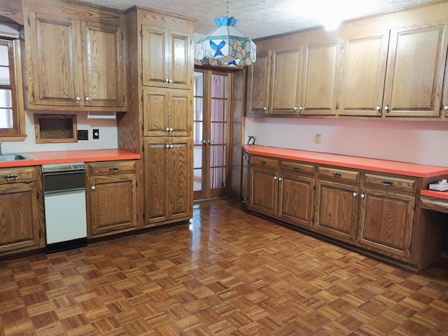 kitchen with a textured ceiling, a sink, light countertops, hanging light fixtures, and brown cabinets