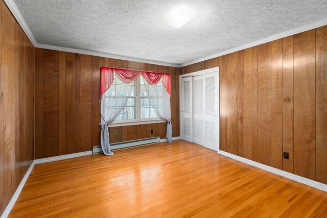 interior space with a textured ceiling, a baseboard radiator, wood finished floors, and wooden walls