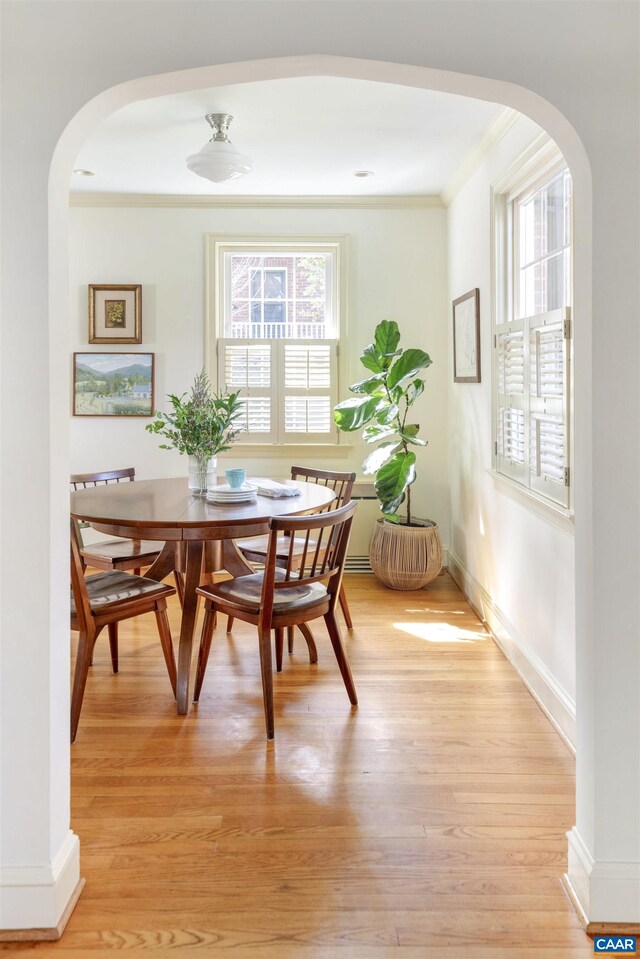 dining area featuring crown molding, light wood-style flooring, arched walkways, and a wealth of natural light