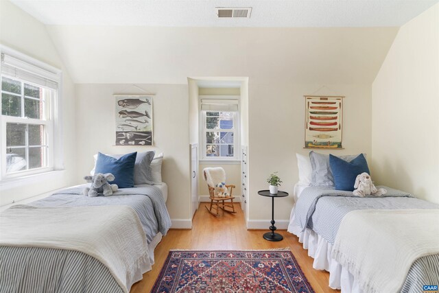 bedroom featuring light wood-style floors, visible vents, lofted ceiling, and multiple windows