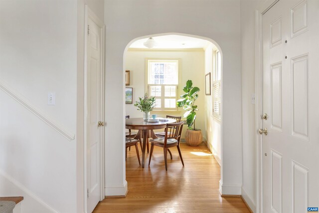 foyer entrance with arched walkways, baseboards, and light wood-style floors