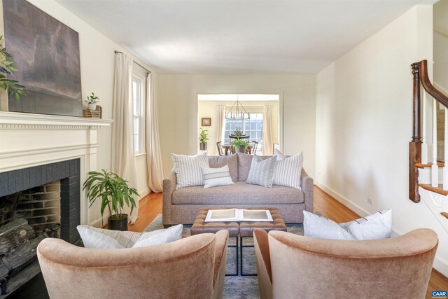 living room with wood finished floors, baseboards, a fireplace, stairs, and a notable chandelier