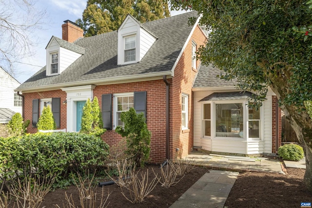 cape cod house with a chimney, brick siding, and a shingled roof