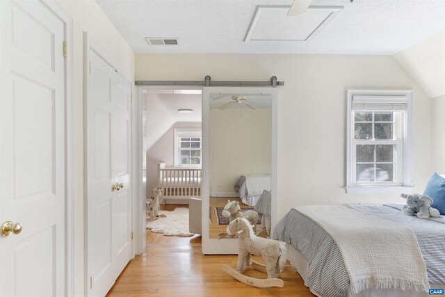 bedroom with visible vents, attic access, lofted ceiling, and light wood-style floors