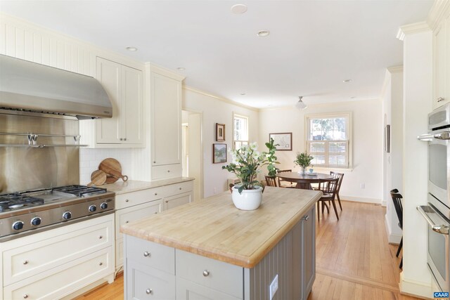 kitchen featuring wall chimney range hood, light wood-style flooring, tasteful backsplash, and stainless steel gas cooktop